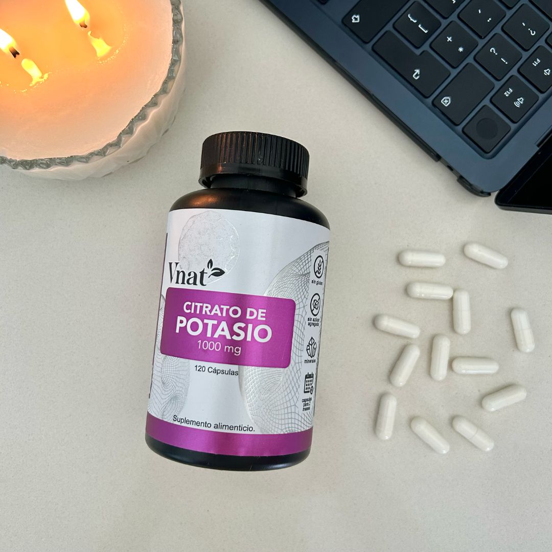 Bote de Citrato de Potasio 1000mg con 120 cápsulas de Vnat al lado de una computadora Mac y una vela aromática con las cápsulas en la mesa para mostrar el tamaño