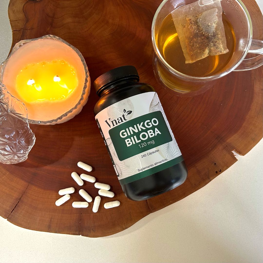 Suplemento de Ginkgo Biloba 120mg con 240 cápsulas de Vnat sobre una tabla de madera con una vela y una taza de té.