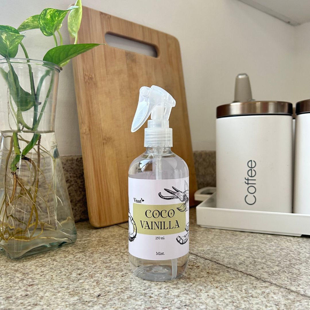 Mist aromatizante de coco vainilla de 250ml en una cocina junto a un jarrón con plantas y un recipiente de café.